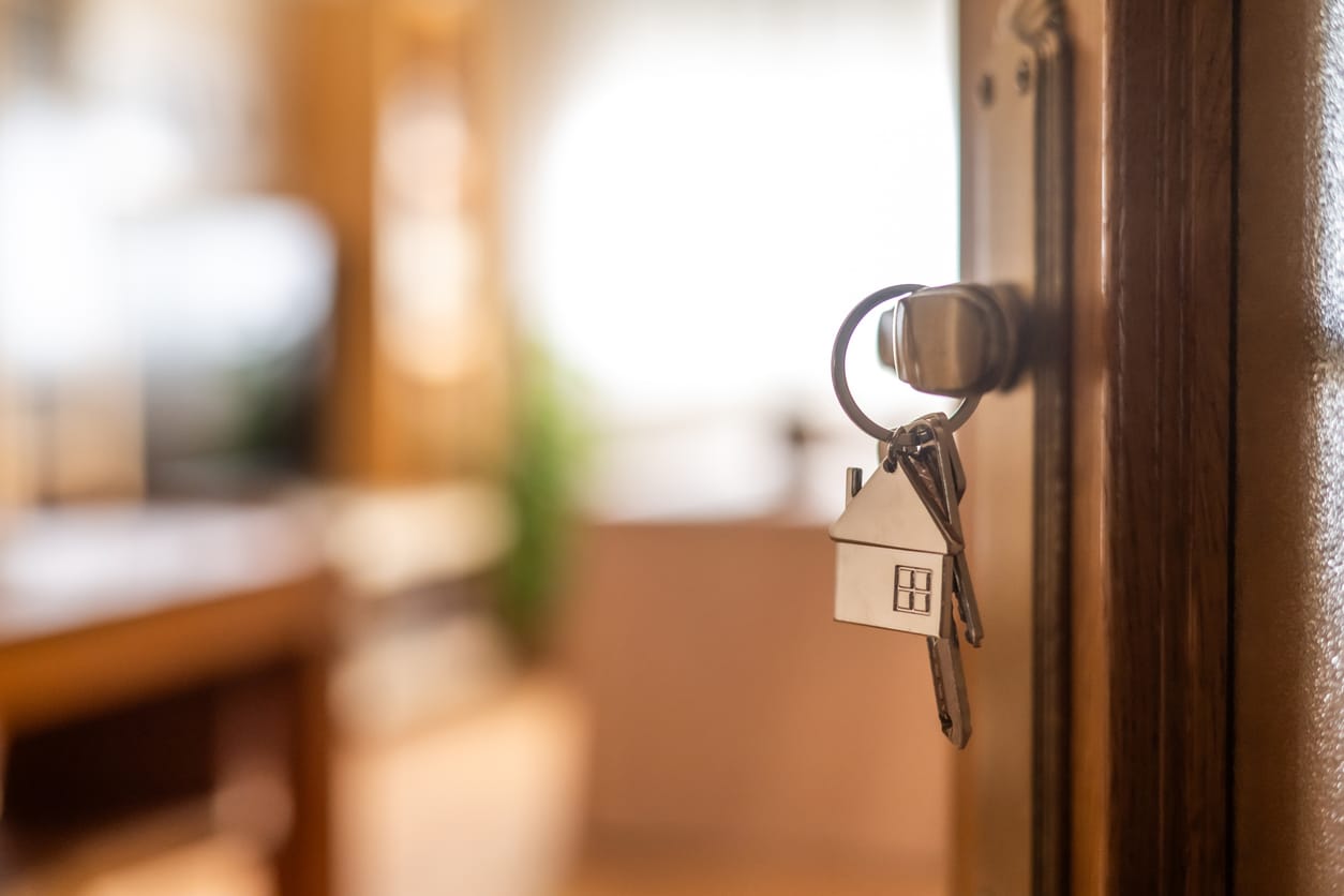 House-shaped keyring hanging from the lock of an open front door